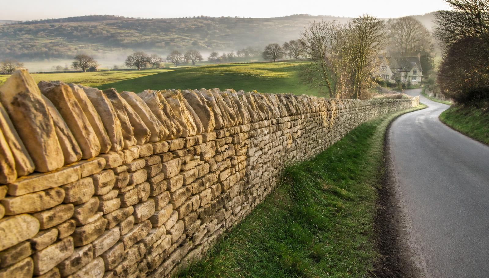 Traditional Cotswold dry stone wall running along a green field boundary in golden light